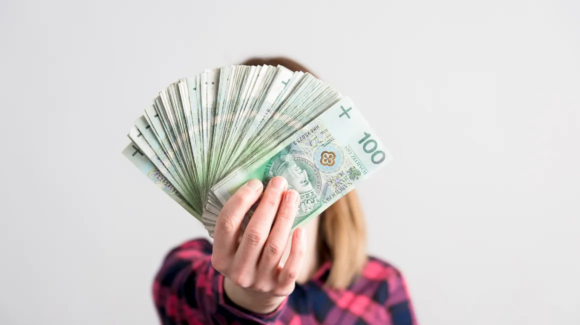 Kobieta trzyma przed twarzą wachlarz z banknotów 100 zł