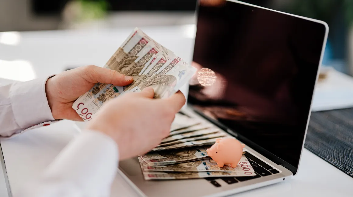Osoba licząca polskie banknoty 500 zł przy laptopie