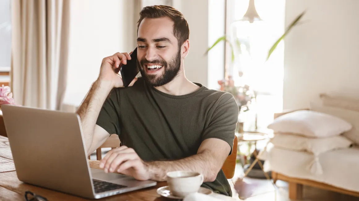 Uśmiechnięty mężczyzna rozmawia przez telefon przy laptopie